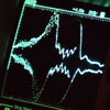 A photo of a computer screen with green lines that form waves on it.
